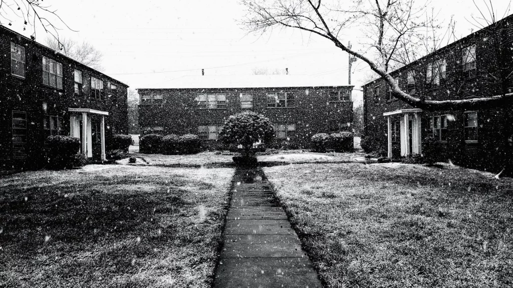 Cover image for “Distance” showing a black-and-white courtyard of apartment buildings in falling snow, with a narrow sidewalk leading toward the center