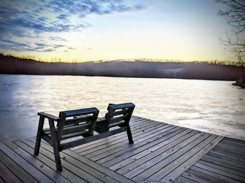 Cover image for “Open Hands” showing two empty wooden chairs on a dock facing a quiet lake at dusk, with winter trees and a fading sky in the distance.