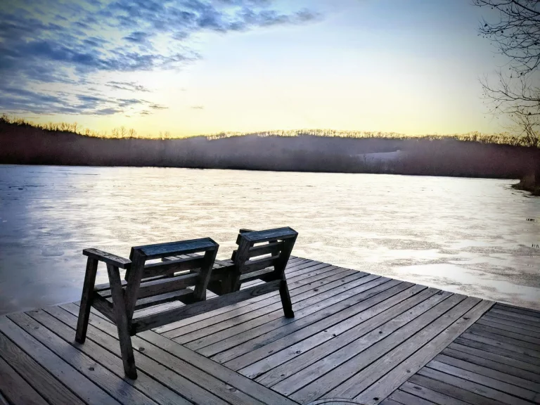 Cover image for “Open Hands” showing two empty wooden chairs on a dock facing a quiet lake at dusk, with winter trees and a fading sky in the distance.